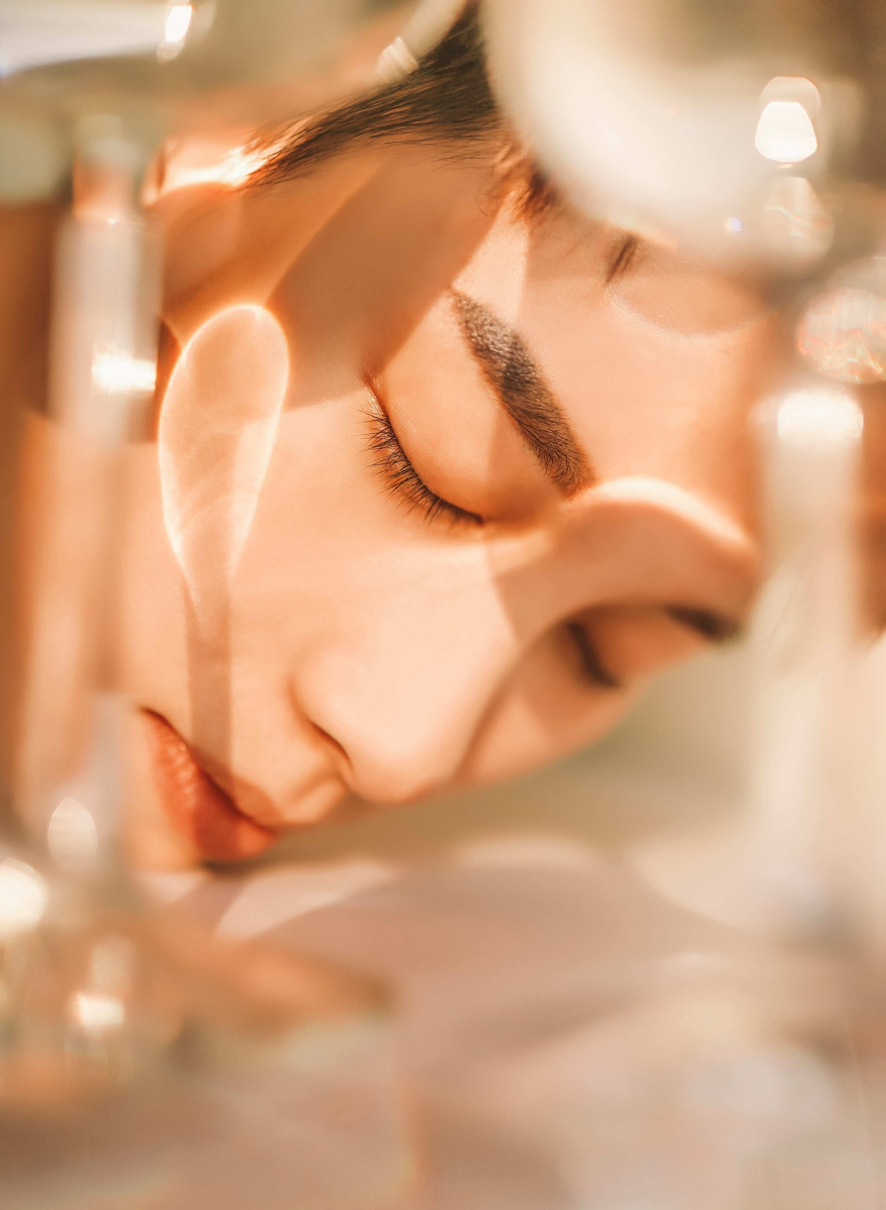 Blurry close-up of face with closed eyes, warm light, abstract reflections.